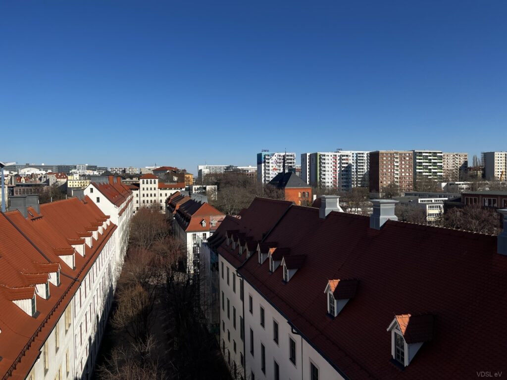 Blick auf eine Stadtlandschaft mit roten Ziegeldächern und modernen Wohngebäuden im Hintergrund.