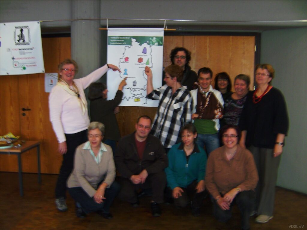 Eine Gruppe von Personen steht vor einer Wandkarte und zeigt auf verschiedene Symbole während eines Spielesymposiums.