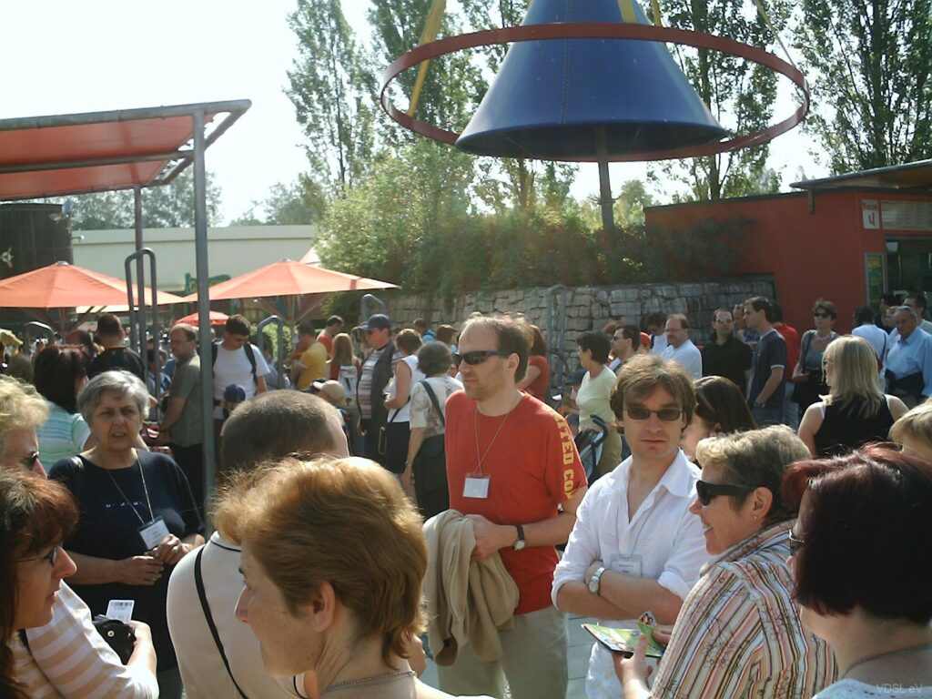 Eine große Gruppe von Menschen versammelt sich im Freien während einer Veranstaltung mit Sonnenschirmen im Hintergrund.