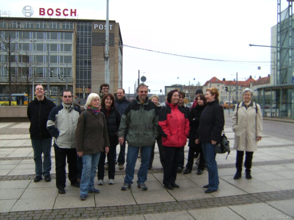 Eine Gruppe von Personen steht auf einem Platz in Leipzig, umgeben von modernen Gebäuden.
