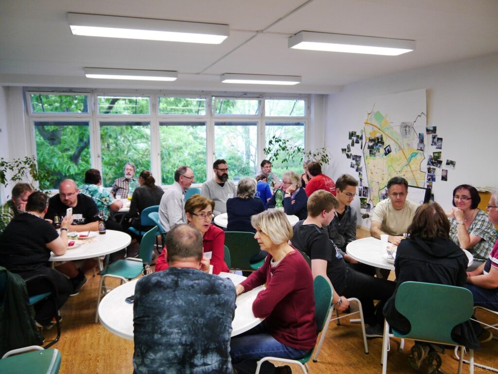 Menschen in einem Raum, die an Tischen sitzen und miteinander diskutieren.