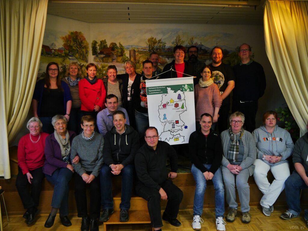 Eine Gruppe von Menschen posiert vor einem Plakat während des Spielesymposiums 2016 in Bielefeld.