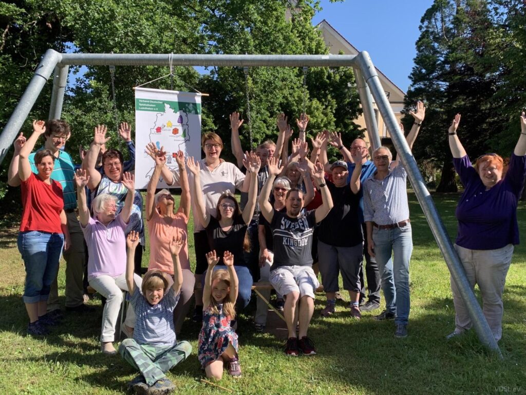 Eine Gruppe von Personen posiert mit erhobenen Händen vor einer Schaukel im Freien.